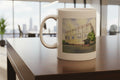White mug with a printed design of a building on a wooden surface with a blurred cityscape background.